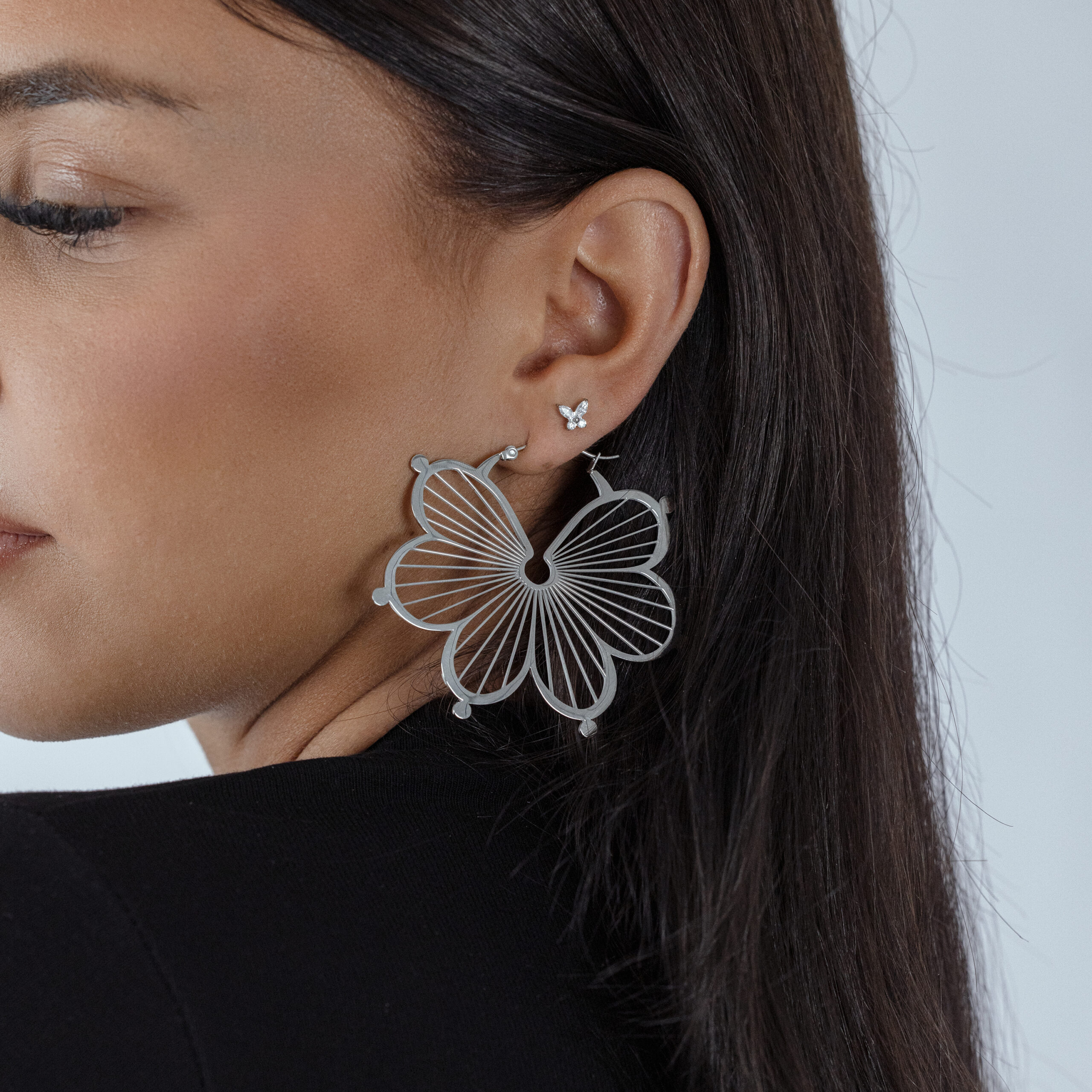 Donna con grande punta a farfalla d'argento nell'orecchio, sfondo nero