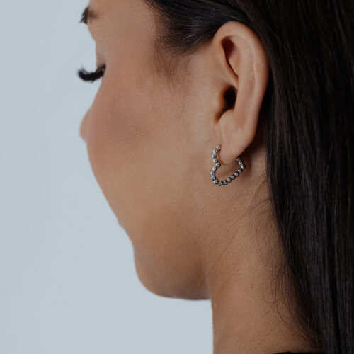 Donna di profilo indossa orecchini a cuore argento su sfondo grigio