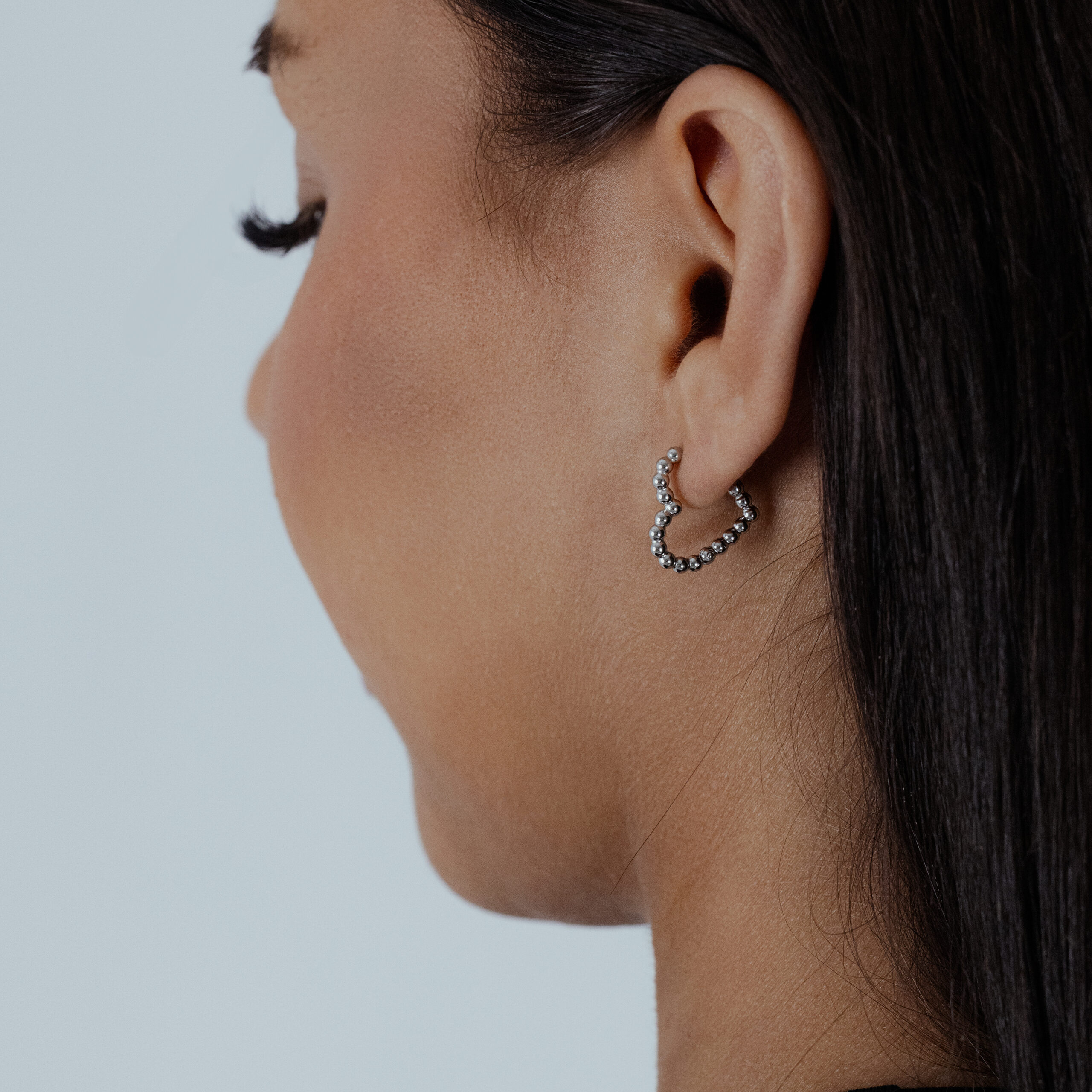 Donna di profilo indossa orecchini a cuore argento su sfondo grigio