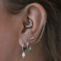 Diversi orecchini nell'orecchio, tra cui Little Tear Hoops neri con cristallo verde.