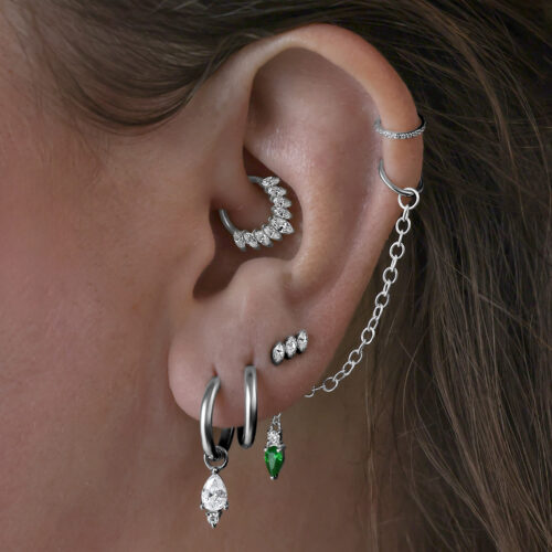 Diversi orecchini nell'orecchio, tra cui Little Tear Hoops neri con cristallo verde.