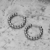 Due orecchini Bubble Hoops argento in acciaio inox su sfondo di cemento grigio