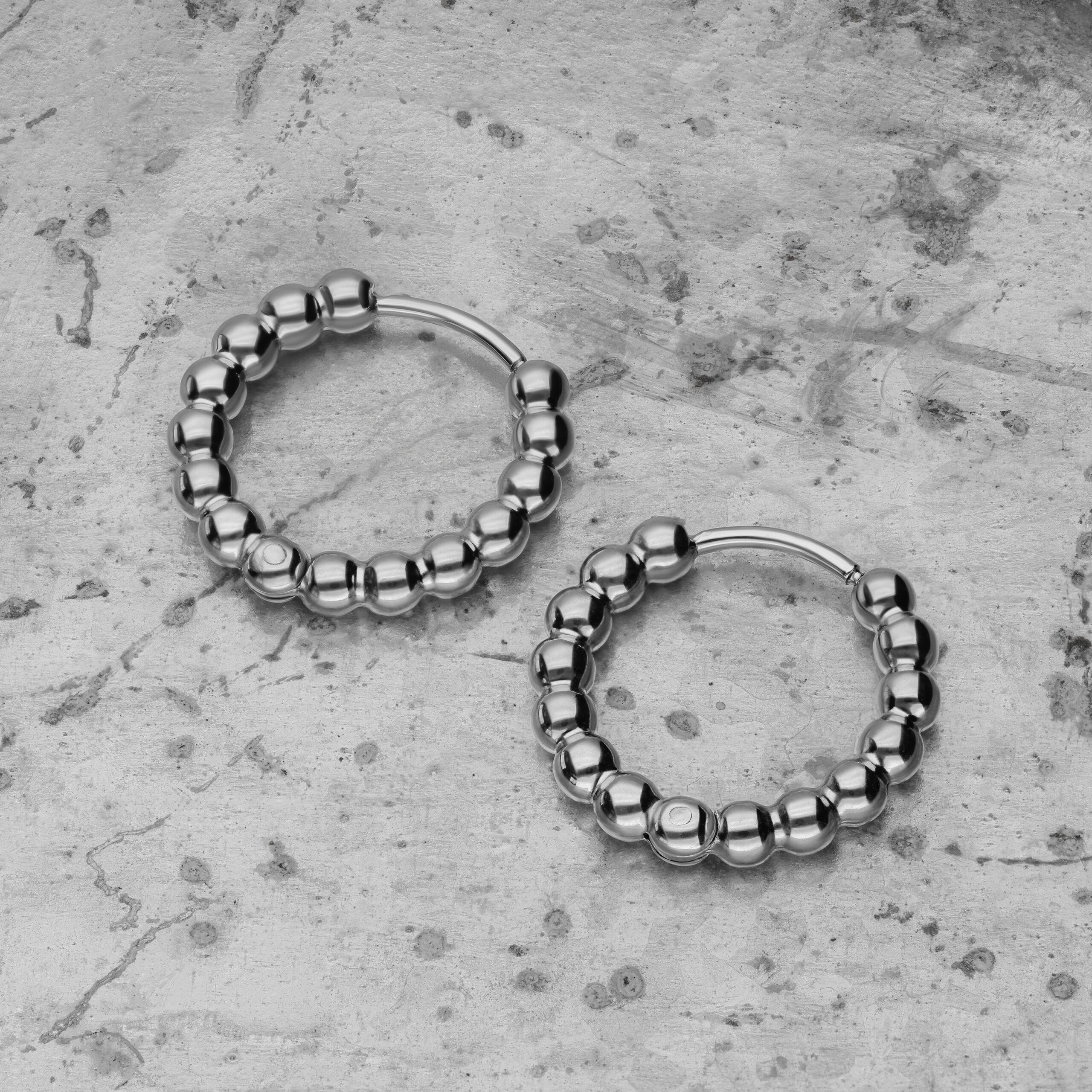 Due orecchini Bubble Hoops argento in acciaio inox su sfondo di cemento grigio
