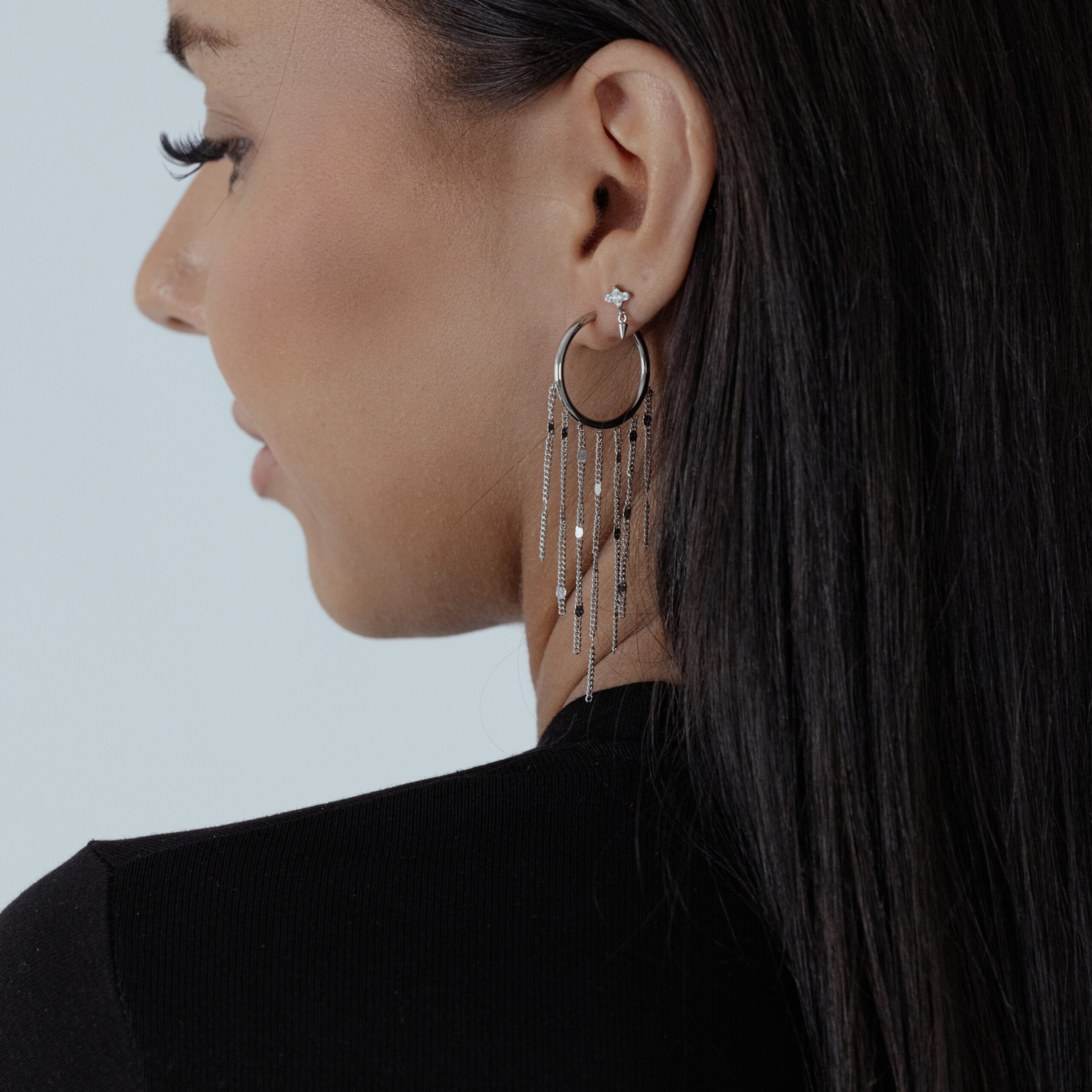 Donna con lunghi capelli scuri indossa orecchini con nappe nere e argento su sfondo bianco