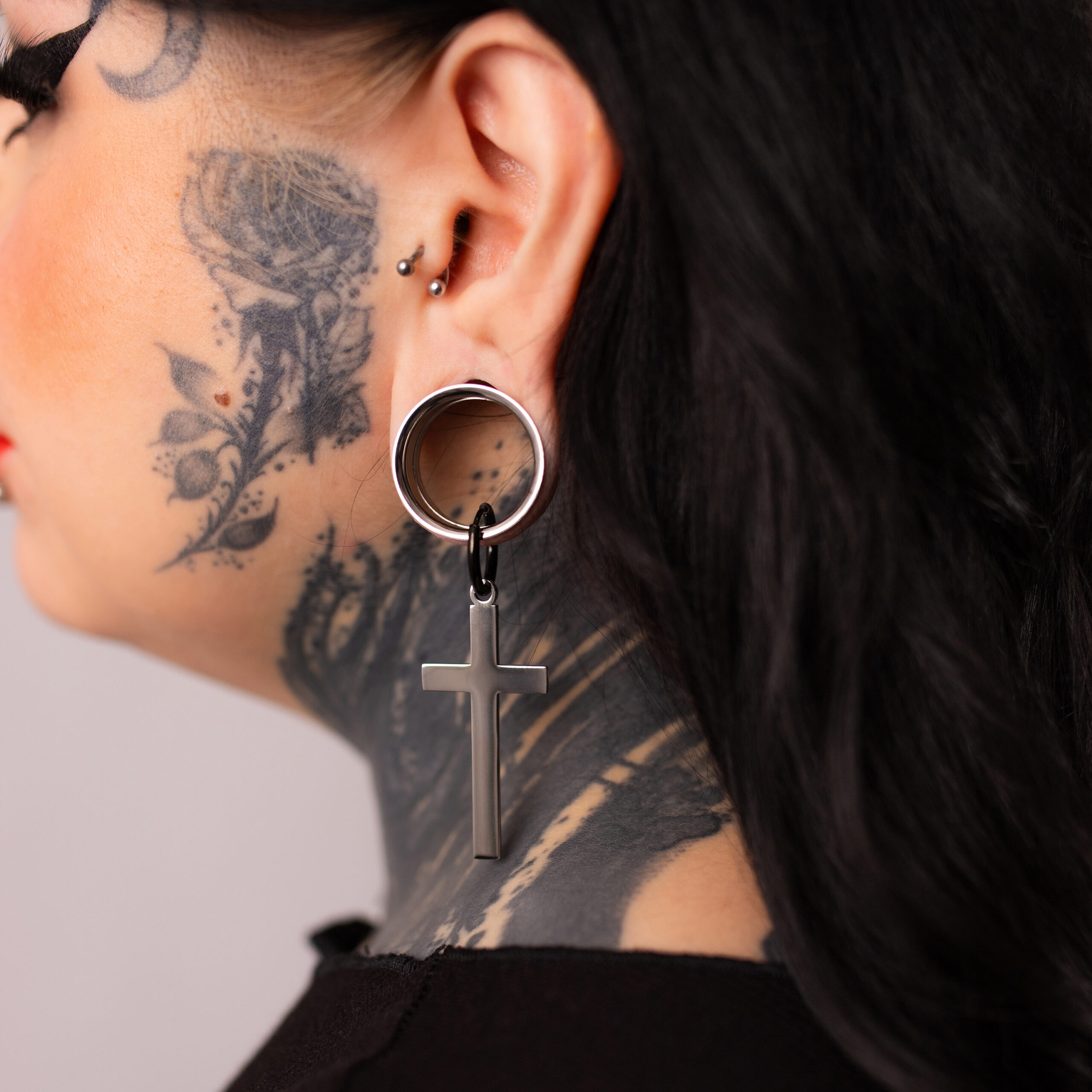 Verena Venus Cross Hoops in argento e nero Orecchini a croce in argento e nero su un orecchio tatuato