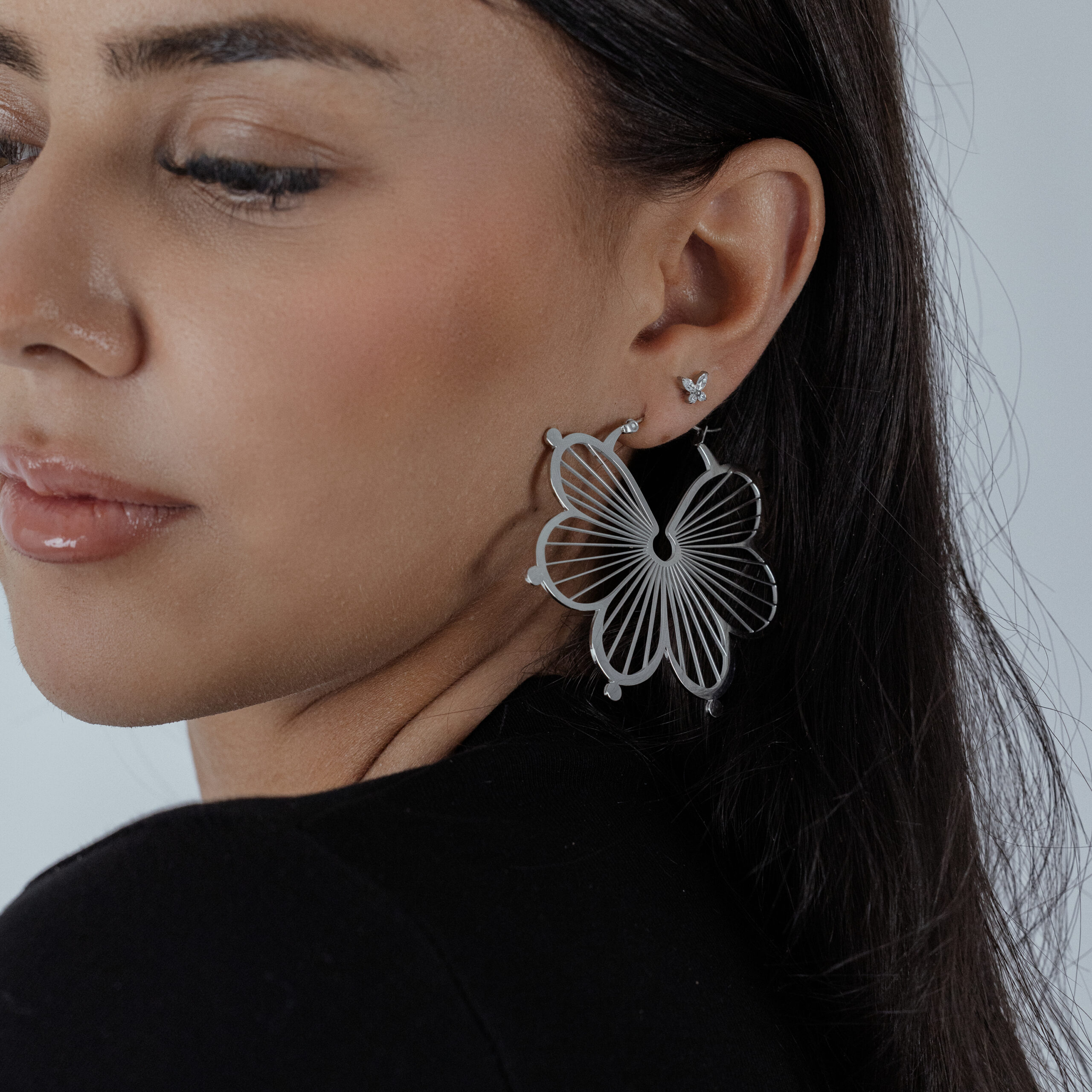 Orecchini a fiore in argento all'orecchio di una donna con top nero, primo piano