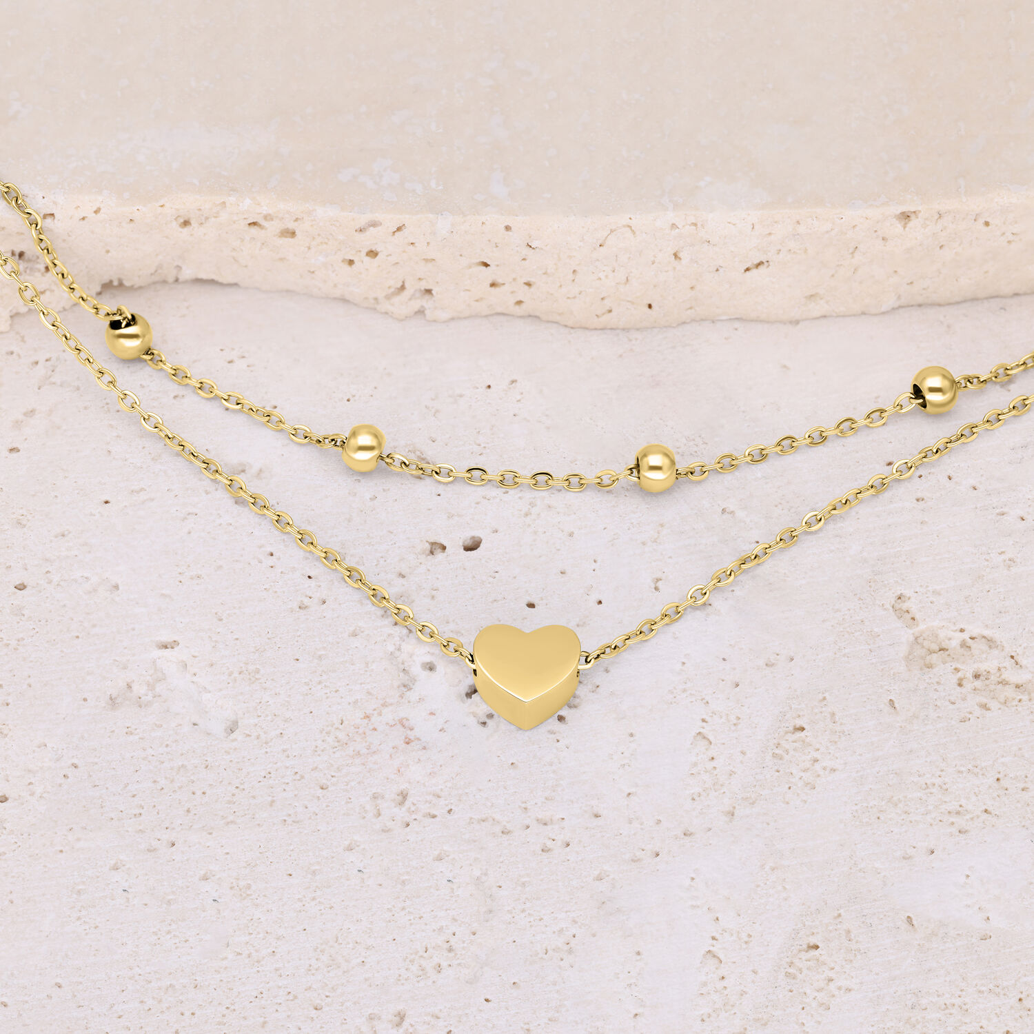Bracciale a doppia fila in metallo dorato con ciondolo a cuore su sfondo beige