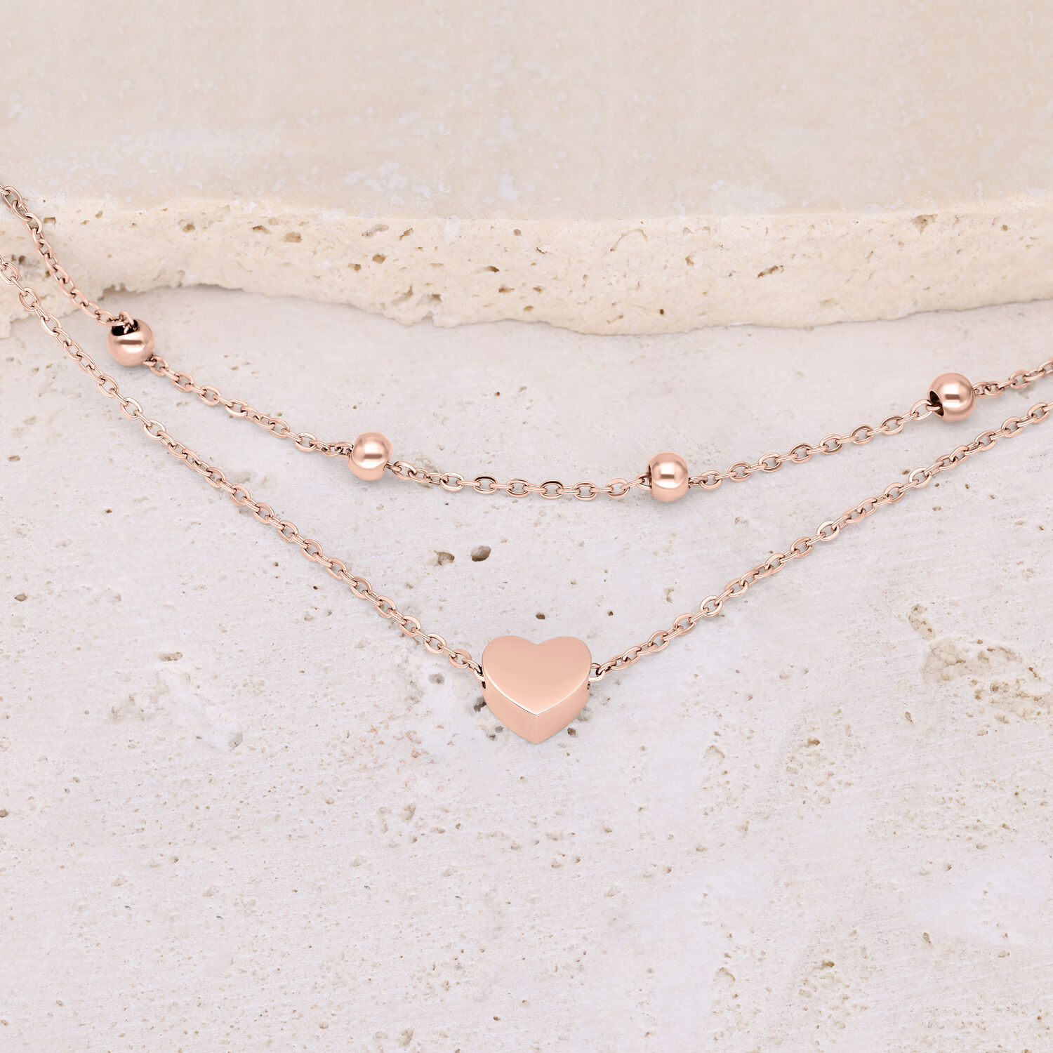 Bracciale a doppio filo in oro rosa con ciondolo a cuore su sfondo chiaro
