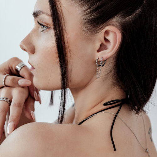 Primo piano di un orecchio con doppi Huggie Ball Hoops neri e argento su sfondo chiaro