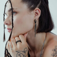 Primo piano di una donna con orecchini a triangolo neri e trecce