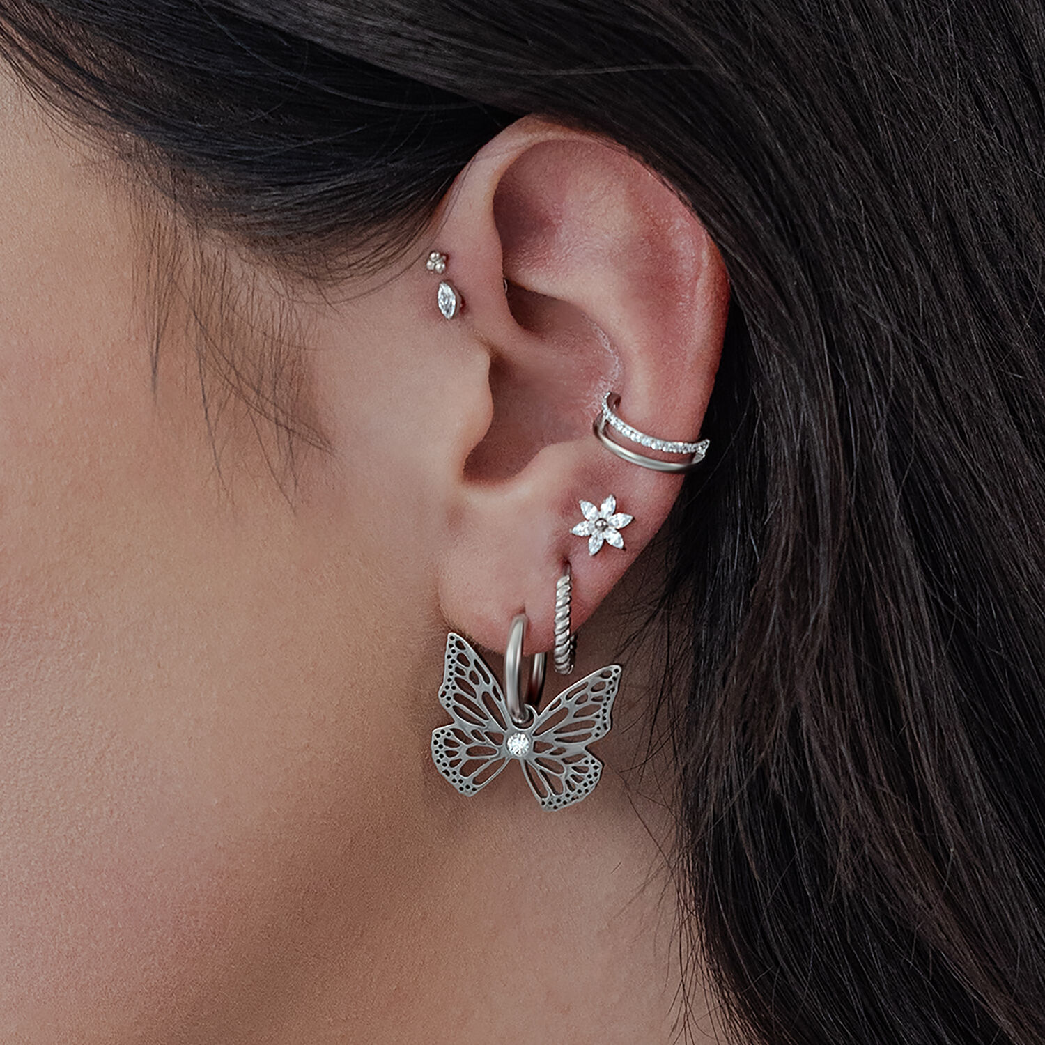 Orecchini Little Butterfly Hoops in argento sull'orecchio di una donna, con altri orecchini a perno