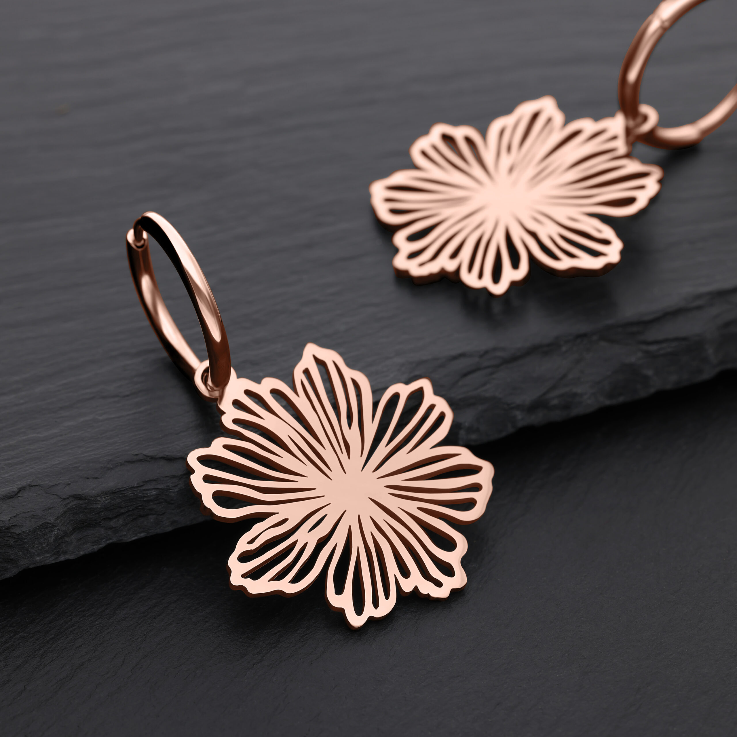 Zwei rosé-goldene Ohrringe in Blumenform auf schwarzem Hintergrund