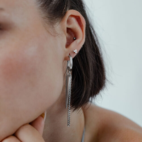 Orecchini a triangolo d'argento all'orecchio di una donna con capelli corti su sfondo chiaro