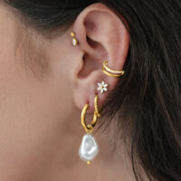 Cerchi dorati con perla barocca all'orecchio di una persona, su sfondo neutro
