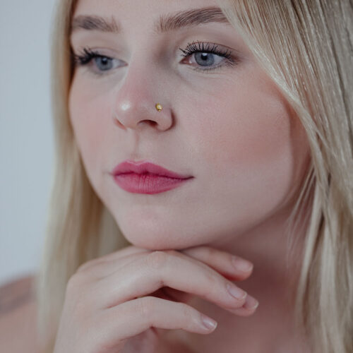 Piercing al naso in oro su una donna, capelli biondi, sfondo neutro