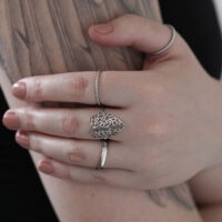 Anello a forma di foglia in argento su una mano tatuata davanti a uno sfondo chiaro