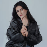 Donna con giacca di pelle nera indossa anello a catena in argento e bracciale abbinato su sfondo grigio