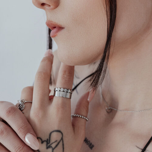 Primo piano di un anello unisex a piastre fini al dito, argento, pelle con tatuaggi sullo sfondo