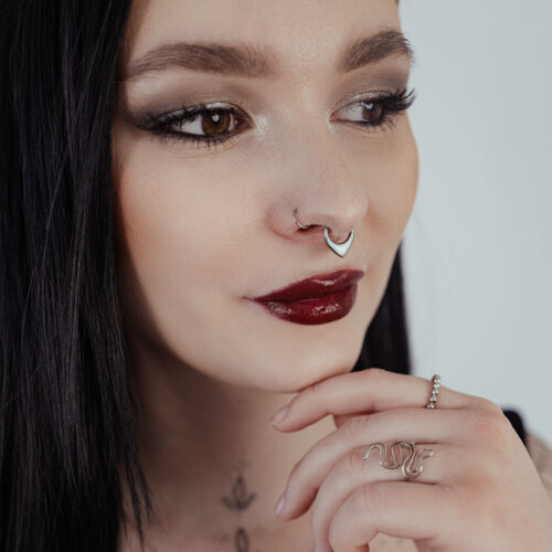 Donna con capelli neri indossa un septum clicker in argento con opale su sfondo chiaro