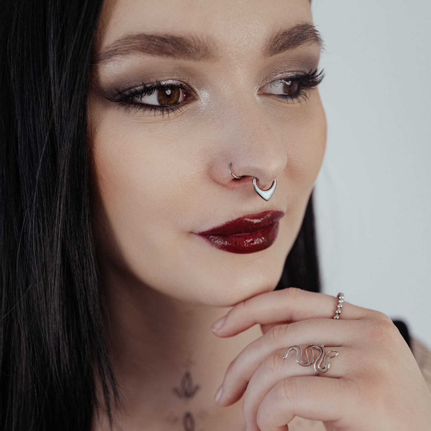Donna con capelli neri indossa un septum clicker in argento con opale su sfondo chiaro