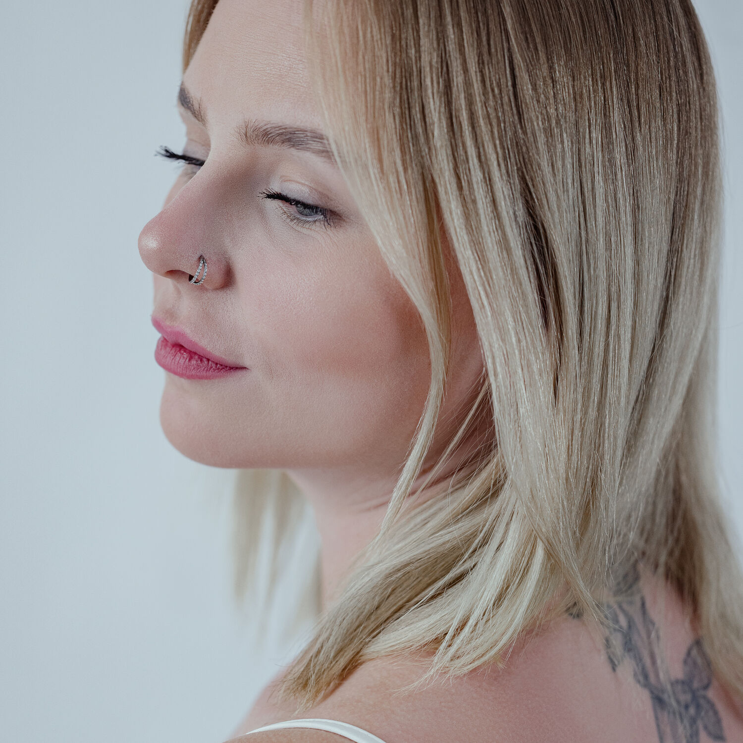 Donna con capelli biondi indossa un clicker nero a doppia fila di cristalli nel piercing al naso su sfondo neutro