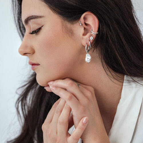 Vista laterale di una donna con orecchini a cerchio con perle barocche e altri orecchini su sfondo chiaro