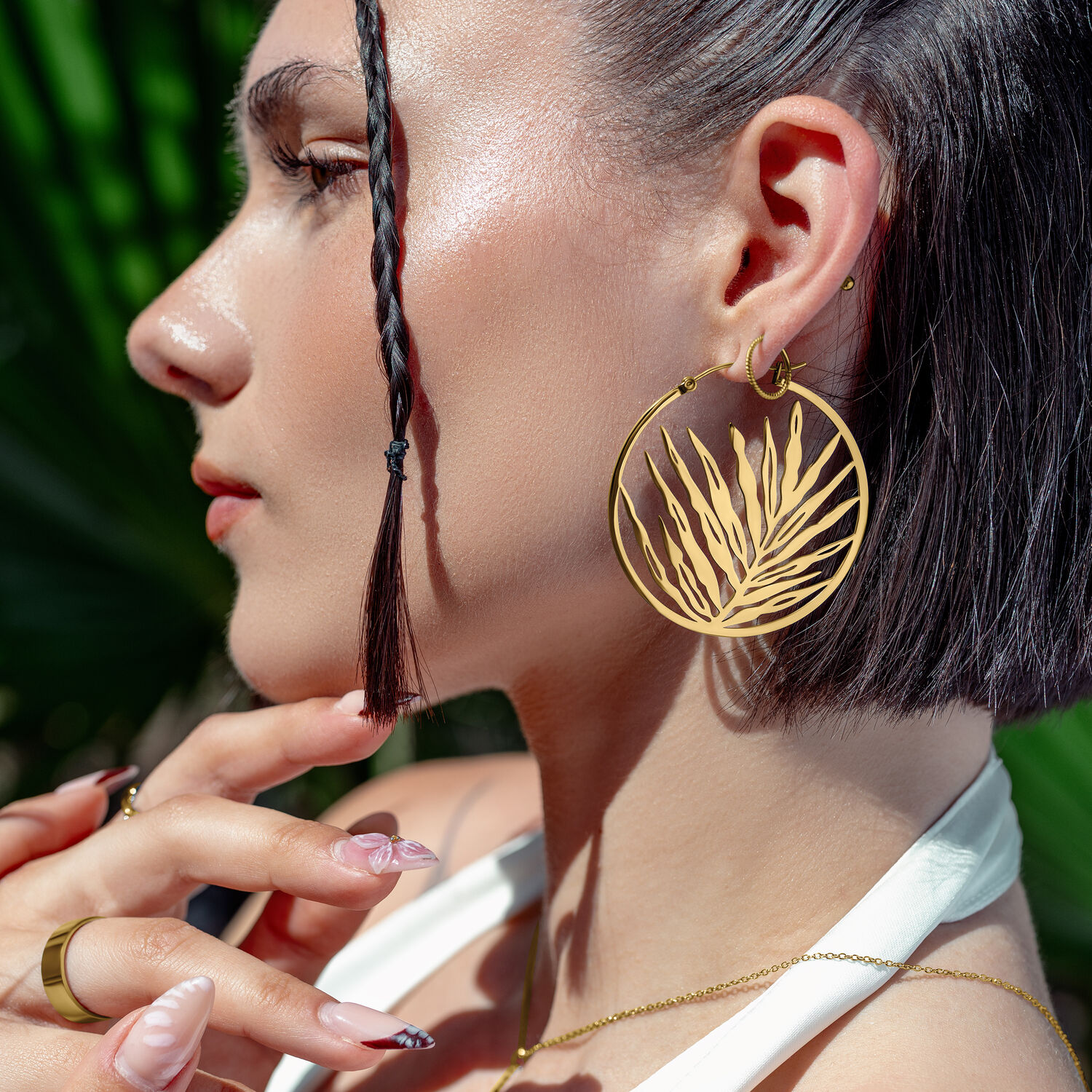 Donna con orecchini Gold Noble Leaf Hoops, di profilo davanti a foglie verdi