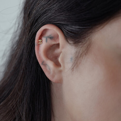 Attacco Cherry in oro indossato all'orecchio da una persona con capelli scuri, su sfondo neutro