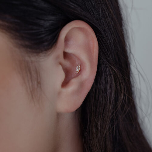 Primo piano di un orecchio con inserto in 14K oro Moissanite su sfondo neutro