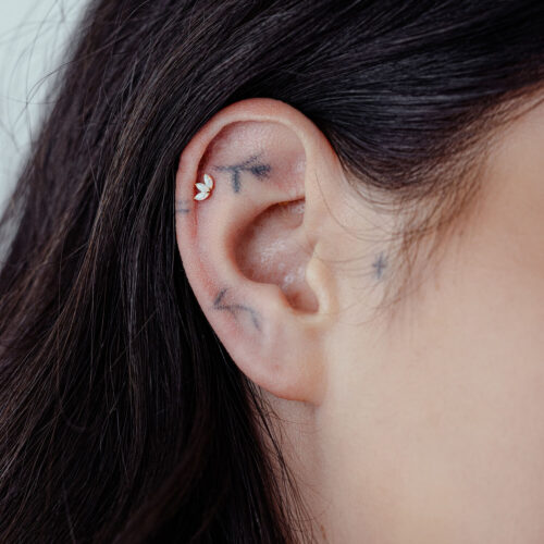 Primo piano di un piercing all'orecchio con loto in oro 14K e opale sintetico su un orecchio