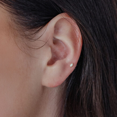 Attacco ovale in oro con opale sintetico nell'orecchio su sfondo chiaro