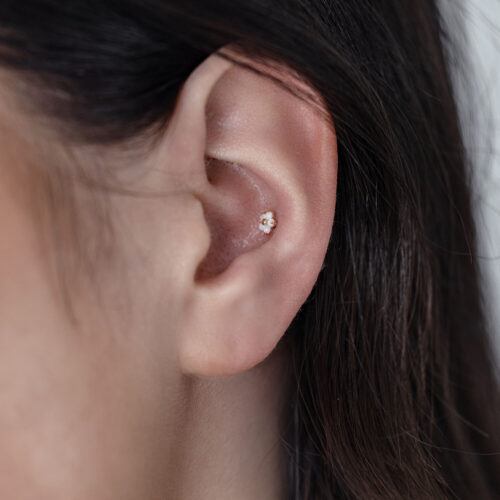 Primo piano di un orecchio con un inserto in oro 14K a forma di fiore con opale