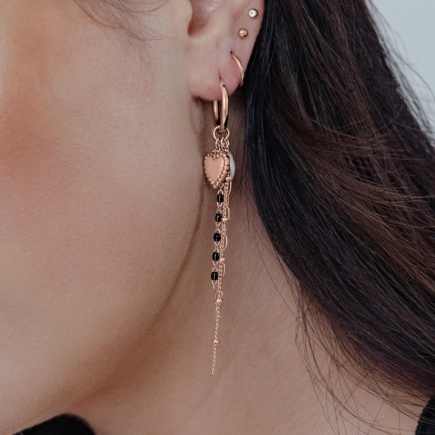 Orecchini a perno in oro rosa con cuore e catena pendente indossati su un orecchio