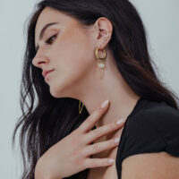 Donna indossa orecchini Gold Edgy Stone Hoops con pietra bianca su sfondo neutro