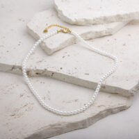 Piccola collana di perle con chiusura dorata Piccola collana di perle sintetiche con chiusura in metallo dorato su sfondo chiaro