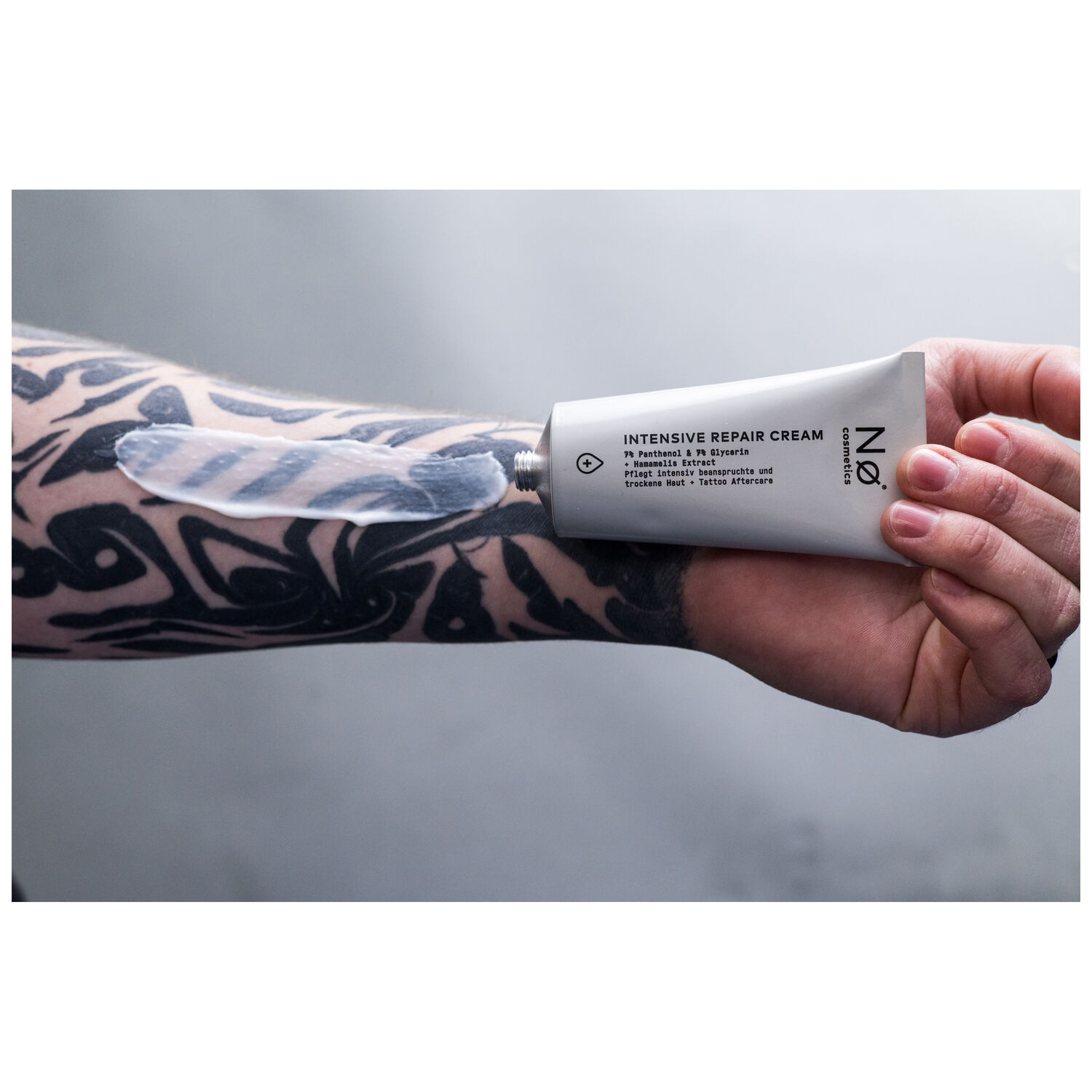 Tubo grigio-bianco della Intensiv Repair Cream di No Cosmetics, tenuto da una mano tatuata