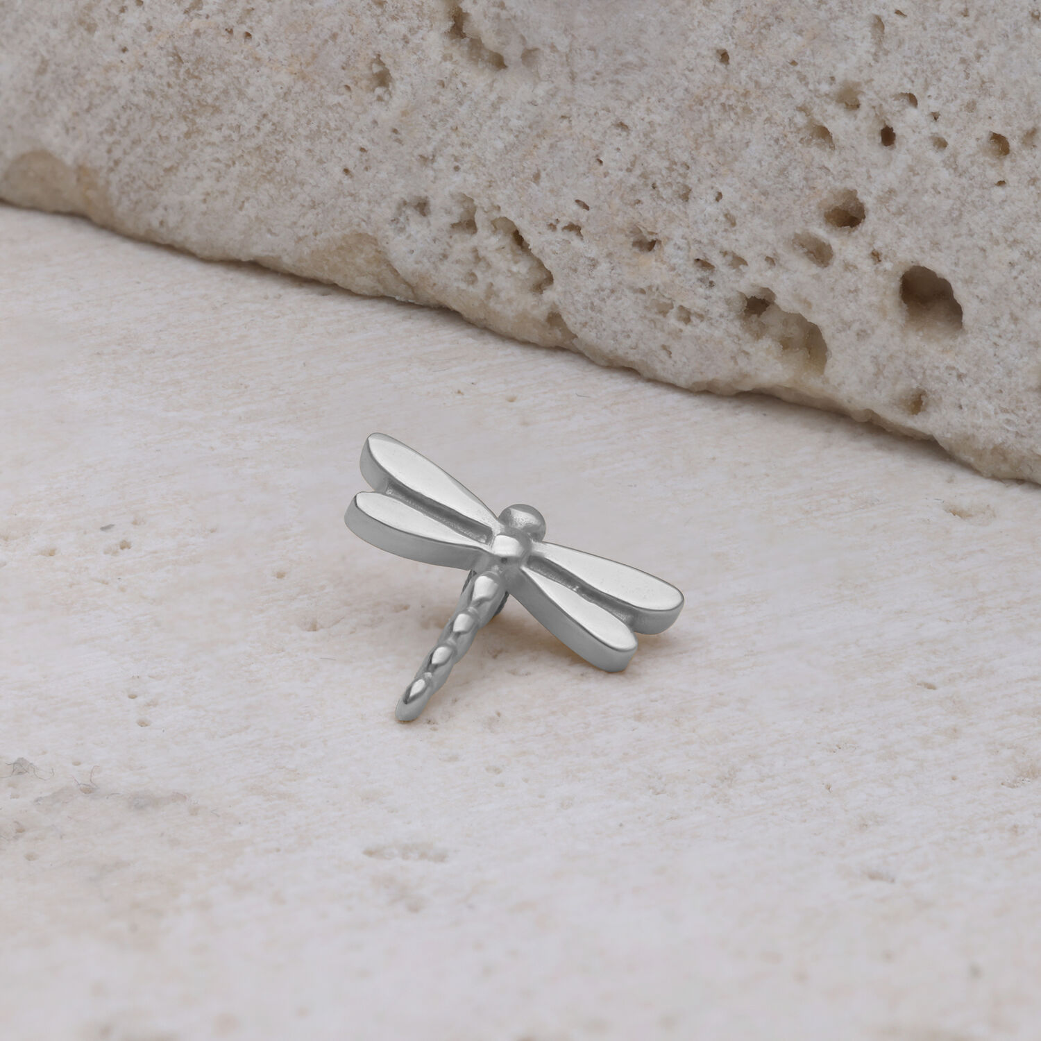 Inserto a forma di libellula in titanio argentato su sfondo di pietra chiara