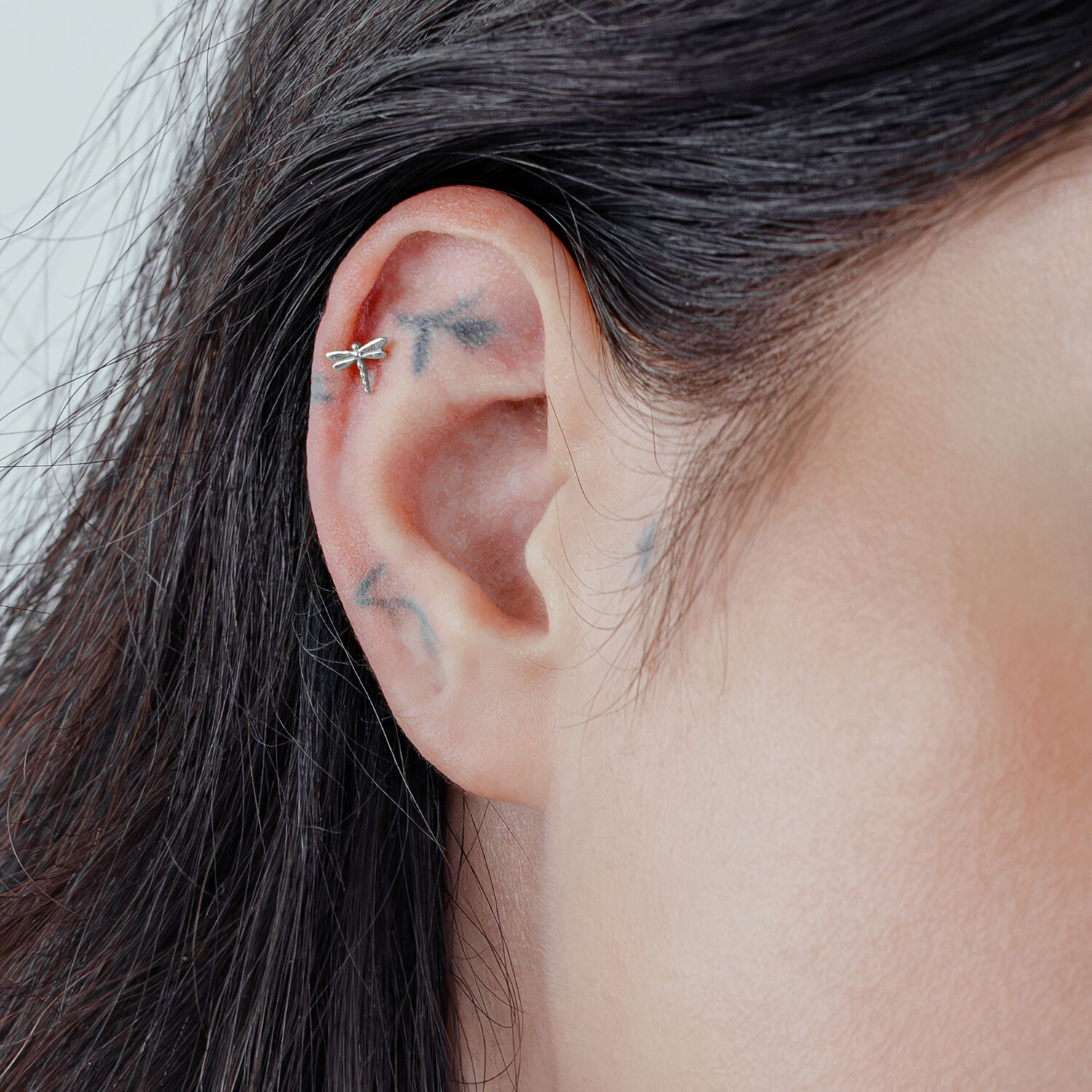 Accessorio a forma di libellula in argento su piercing all'orecchio su sfondo chiaro