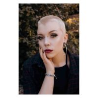 Persona con cono piercing in titanio argento e capelli corti davanti a un fondale di foglie