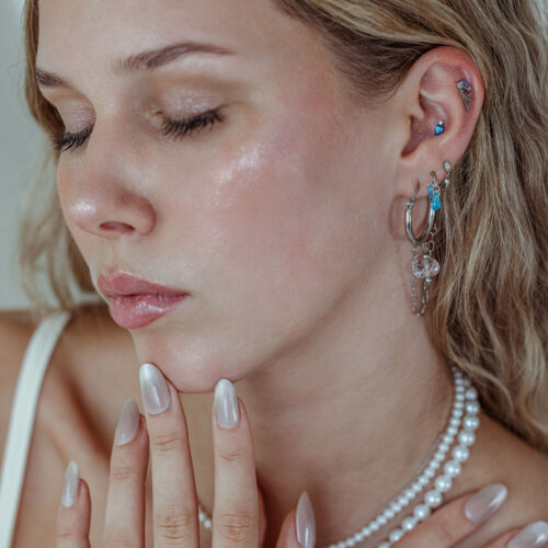 Donna con diversi piercing all'orecchio, incluso l'attacco Mystic Dew in argento e oro con cristalli color lavanda e turchese, su sfondo neutro