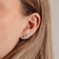 Primo piano di un orecchio con disco d'argento per Triple Piercing di 4,0 mm su sfondo chiaro