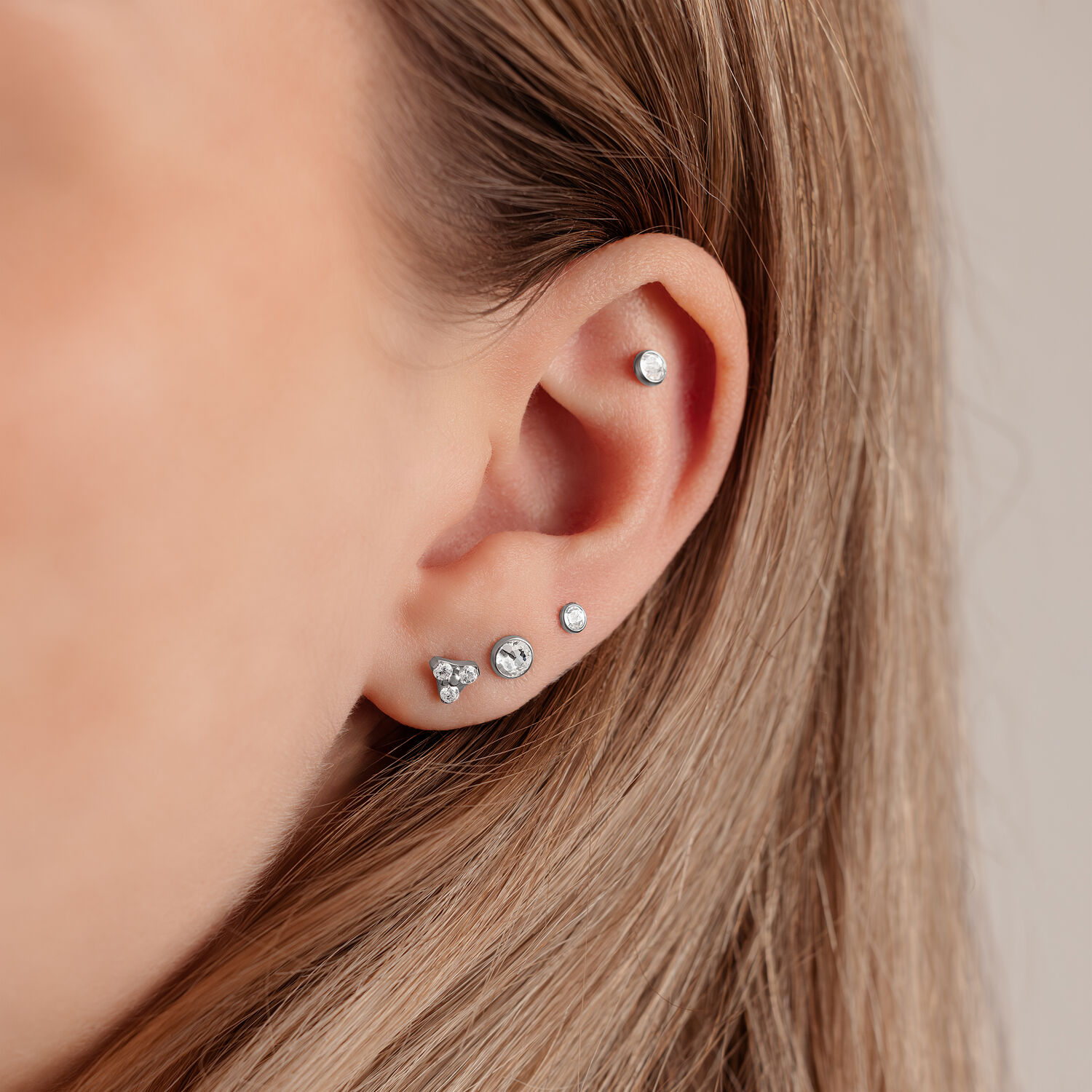 Primo piano di un orecchio con disco d'argento per Triple Piercing di 4,0 mm su sfondo chiaro