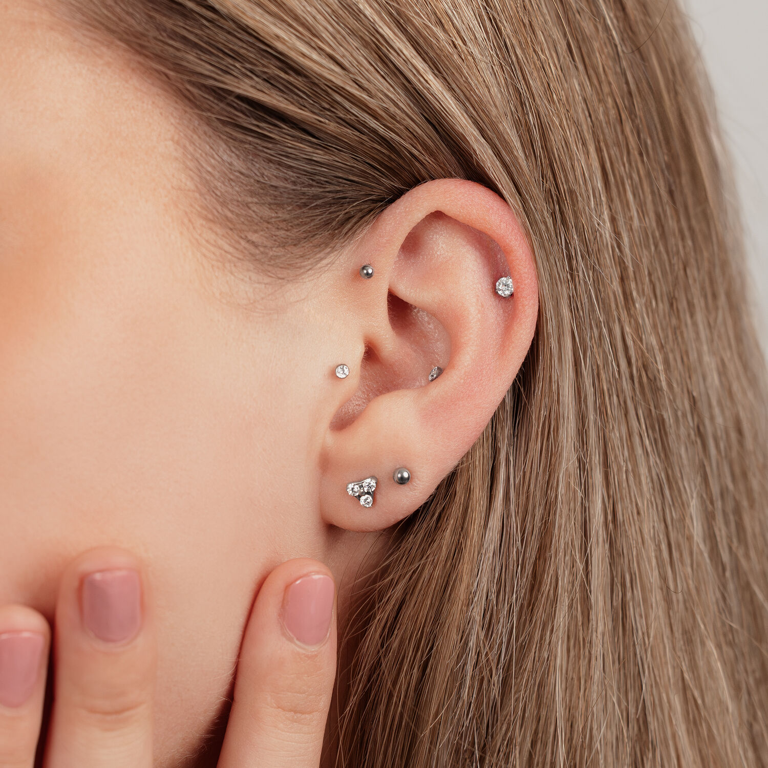 Primo piano di un orecchio con diversi piercing in titanio nero e argento