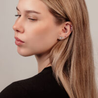 Donna con diversi piercing e orecchino a sfera di cristallo su sfondo chiaro