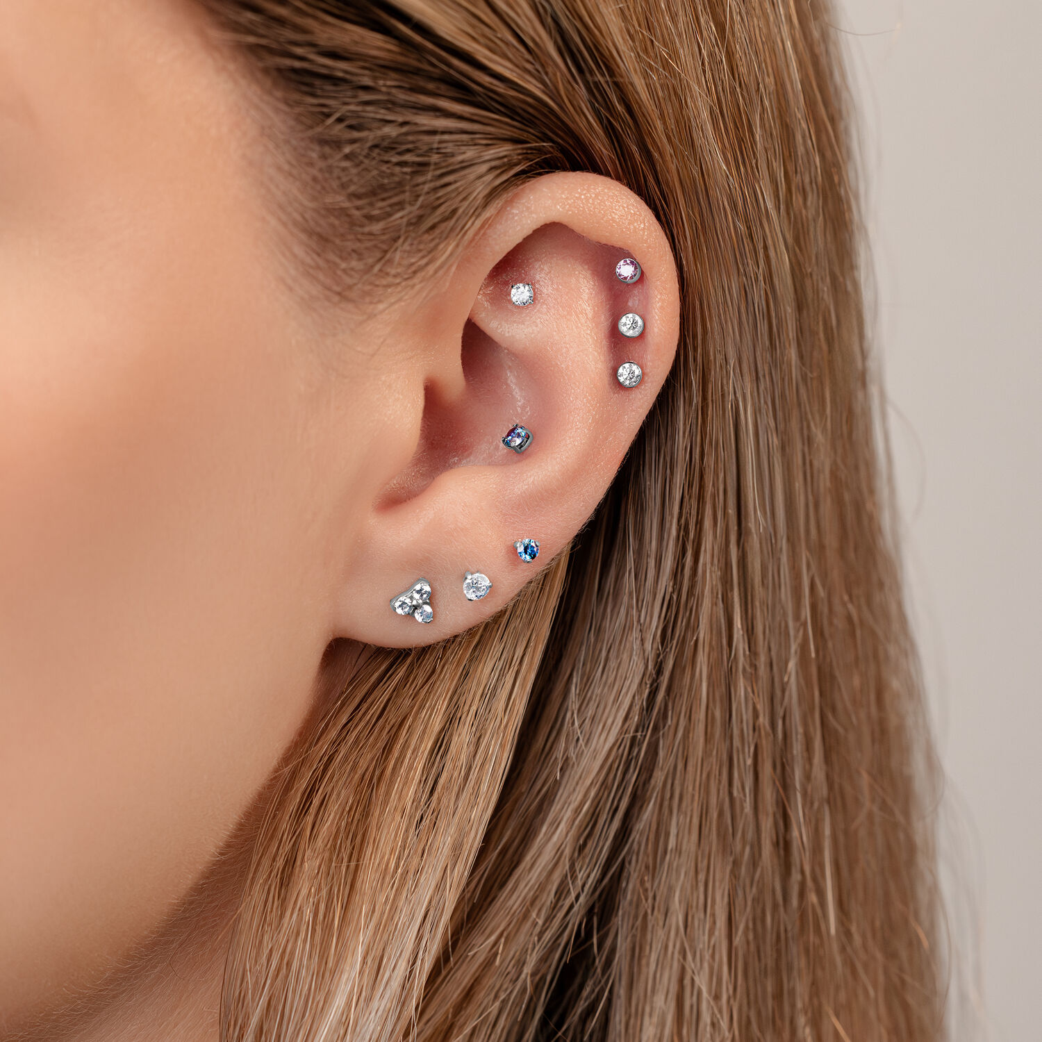 Primo piano di un orecchio con più piercing, incluso un attacco a 3 punte in colori cristallo