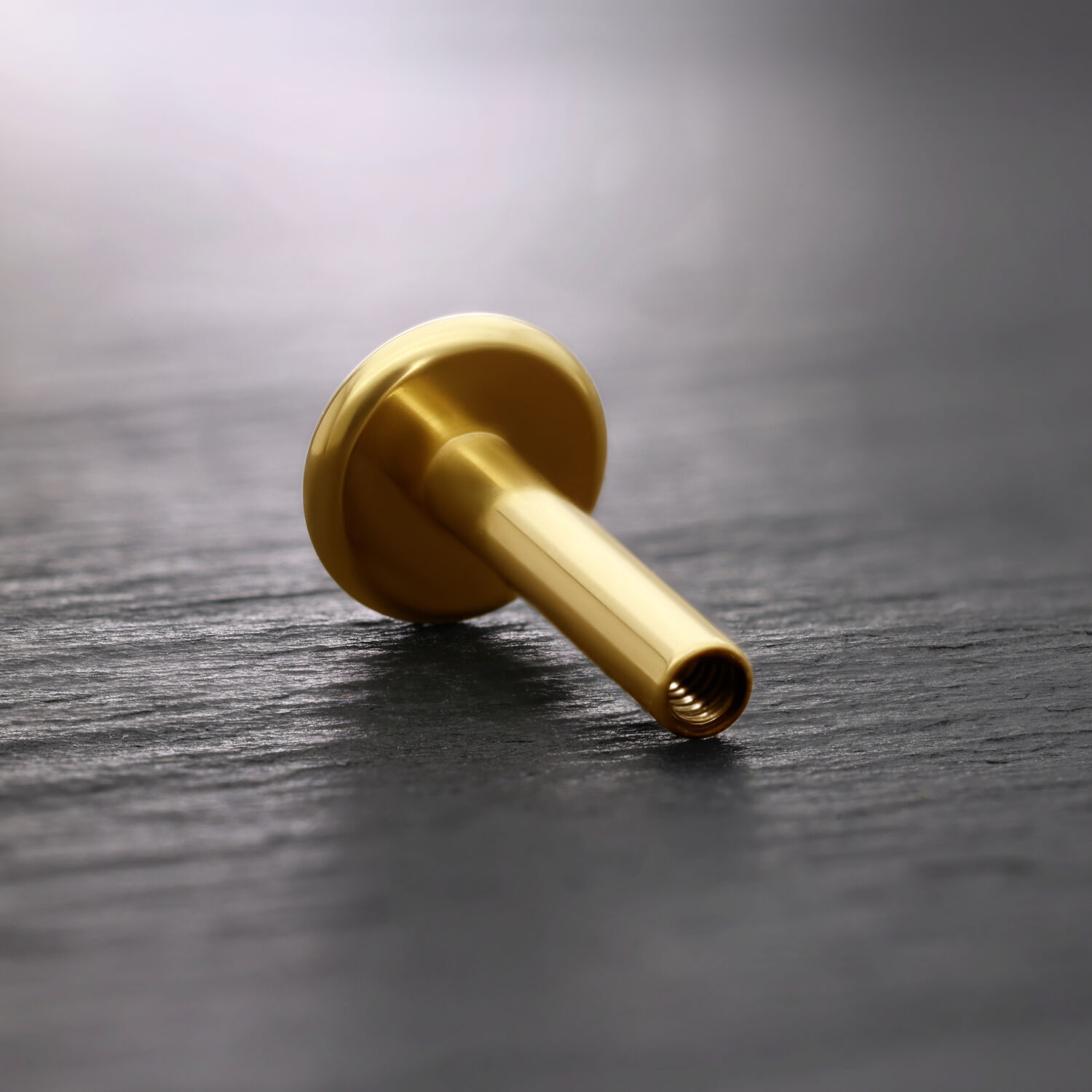 Labret in titanio dorato su sfondo scuro, inclinato