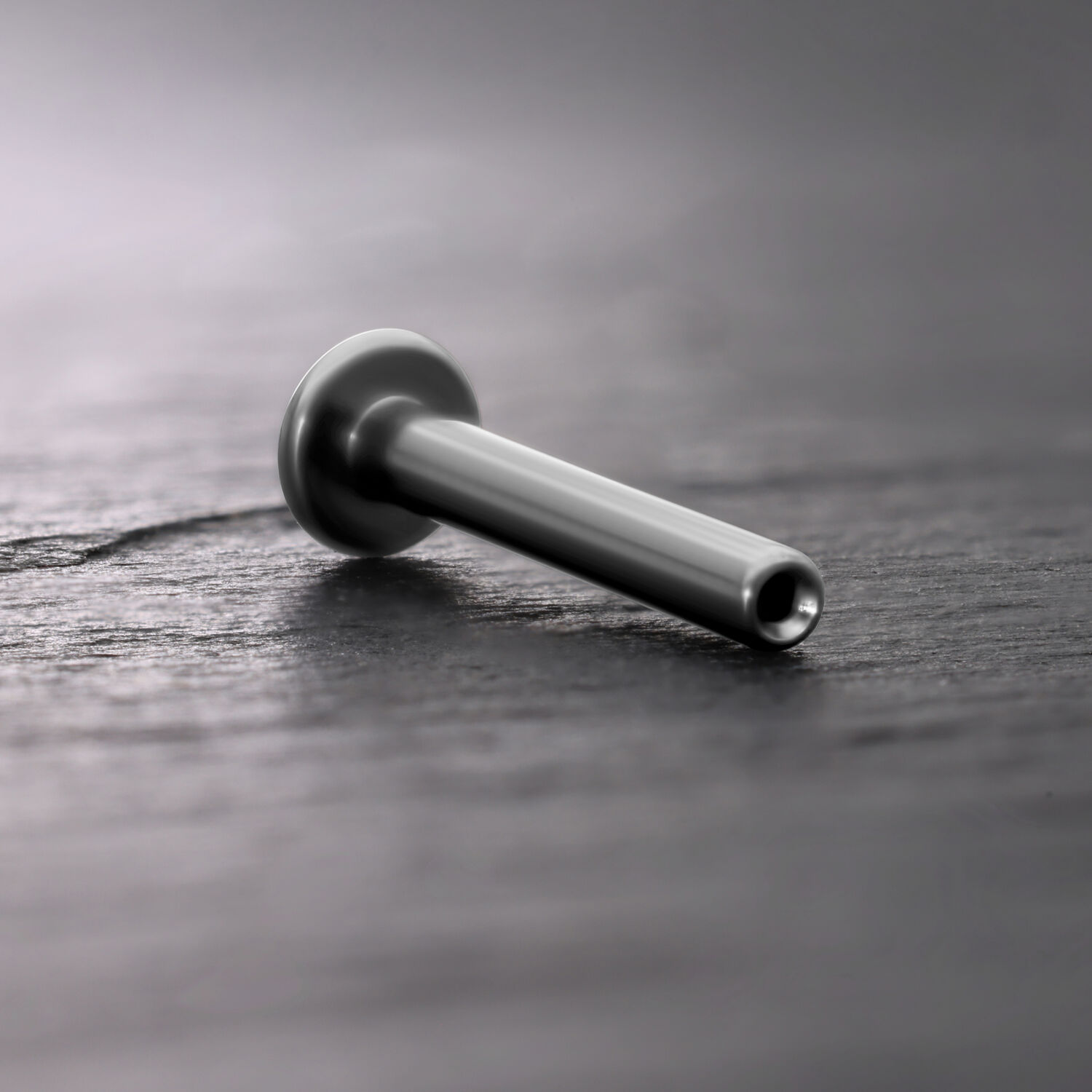 Labret Push Fit in titanio argento su sfondo di legno scuro
