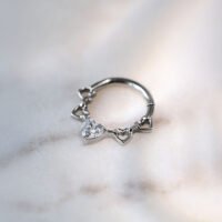 Clicker per setto nasale in titanio argentato con design a cuore e cristalli su sfondo marmorizzato