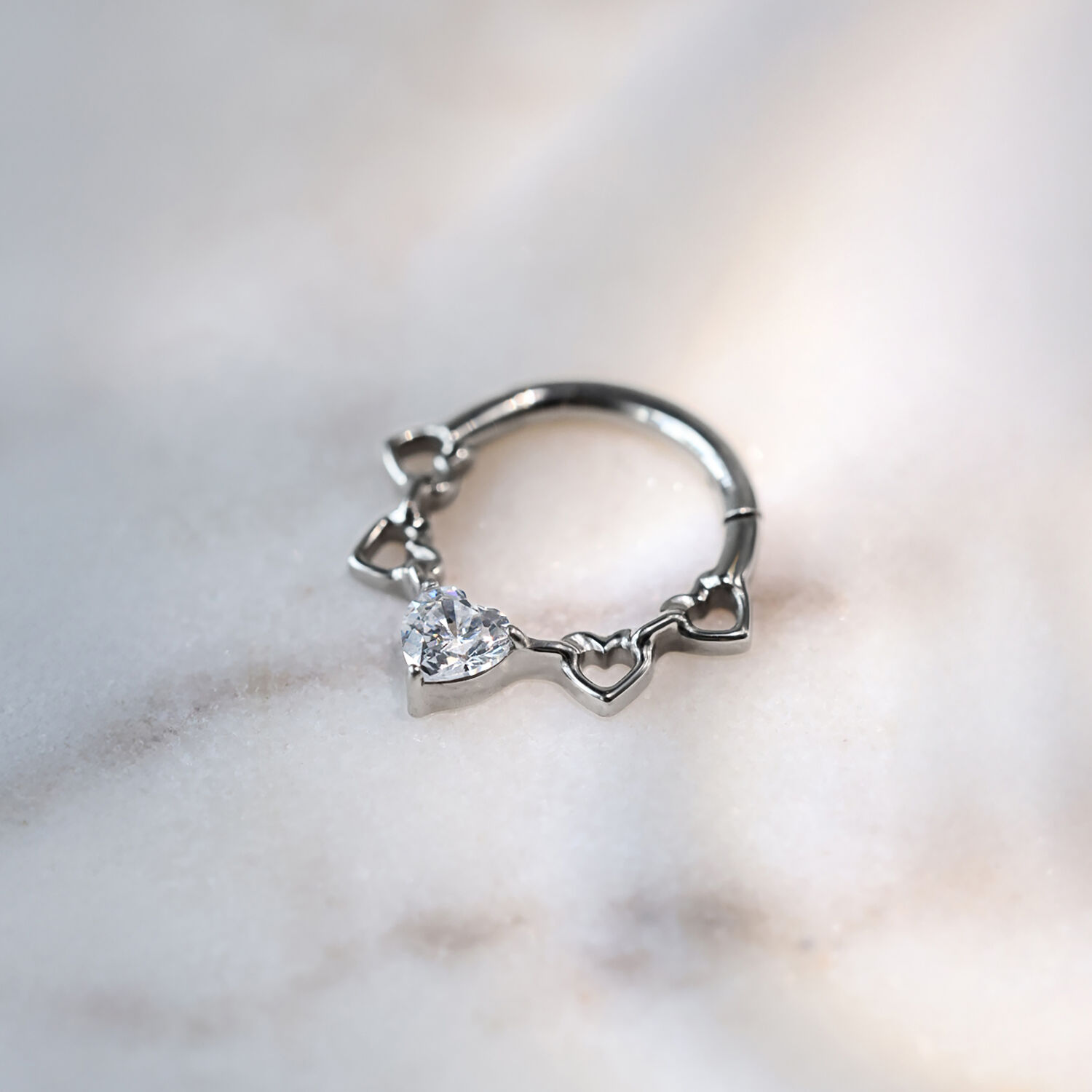 Clicker per setto nasale in titanio argentato con design a cuore e cristalli su sfondo marmorizzato