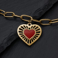 Bracciale in metallo dorato con ciondolo a forma di cuore e cuore rosso su sfondo ardesia